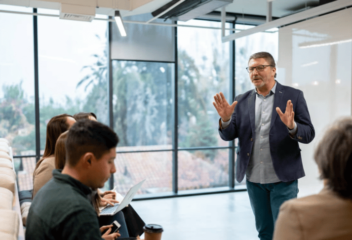 A busy, modern office scene with a group of professionals collaborating around a computer displaying financial data, while others work in the background.