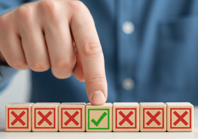 A finger points to a wooden block with a green checkmark, surrounded by other blocks with red 'X' marks.