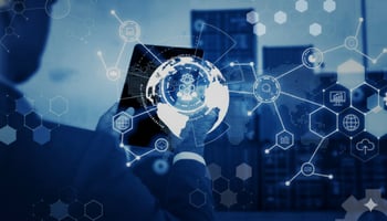 A businessman holds a tablet displaying a global network of interconnected digital icons, overlaying a background of shipping containers, suggesting global logistics and technology.