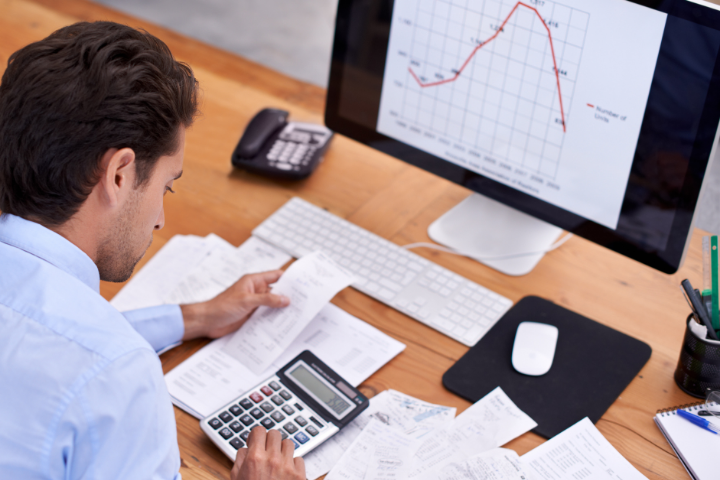 An employee working at his desk with a calculator and an image of a graph.