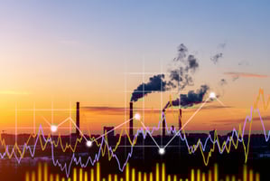 ndustrial factory at sunset with smoke rising from chimneys, overlaid with colorful financial graphs representing manufacturing performance data.