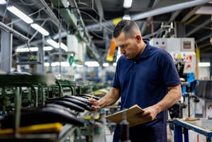 A worker with an orange vest and earmuffs holding a wrench.