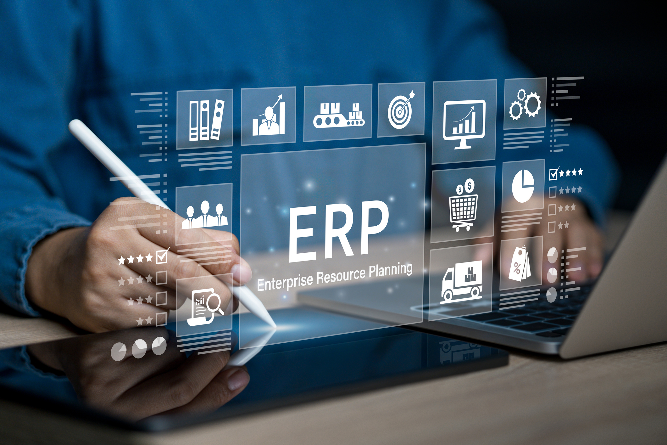 Person using a stylus and laptop with a digital interface displaying ERP icons representing business functions such as analytics, supply chain, sales, and finance.
